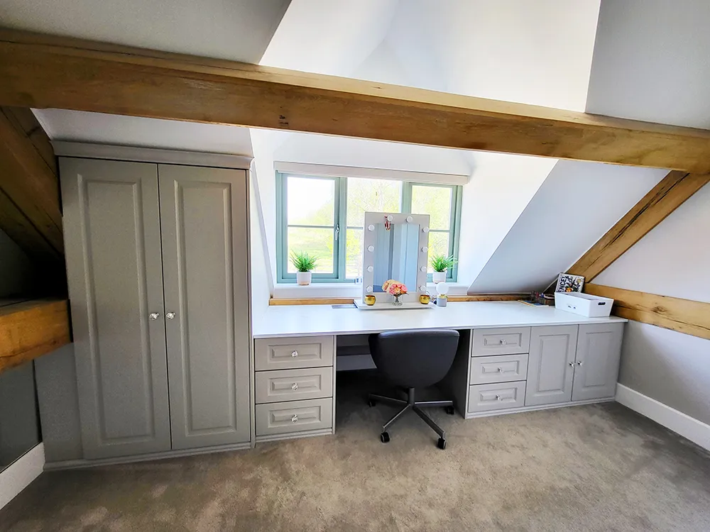 White dressing table under bedroom window with carpet adn oak beams.