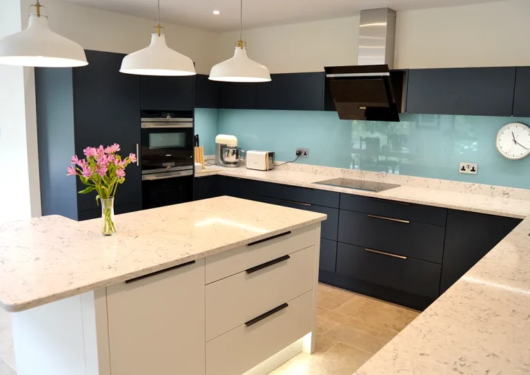 A kitchen with white and dark blue cupboards, marble work surface and a light blue splashback.
