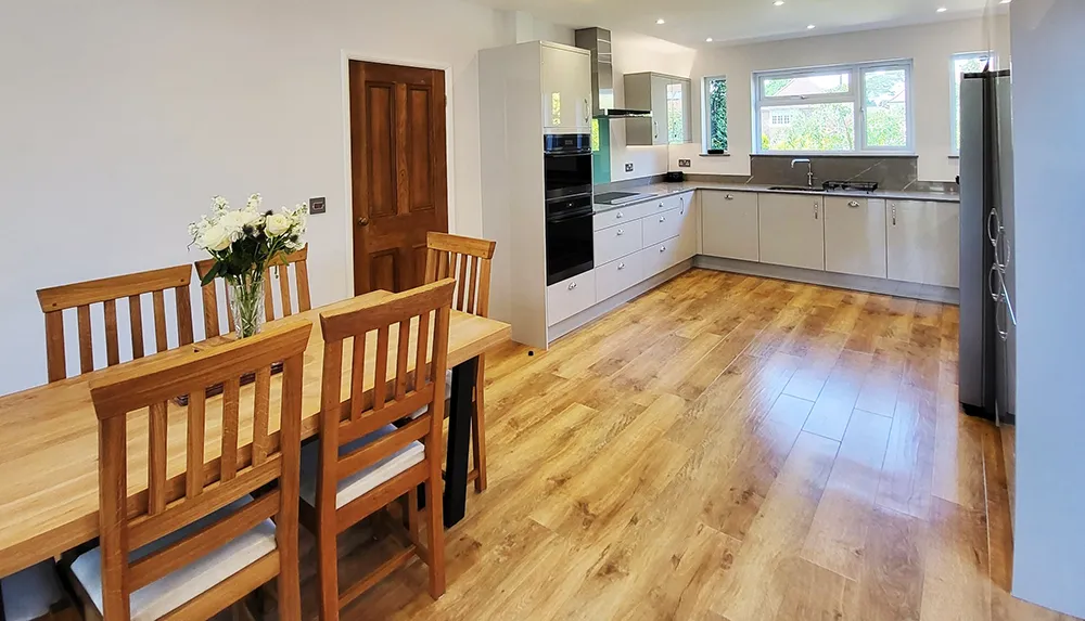 Open plan kitchen with wooden floors, dining table and white kitchen units.