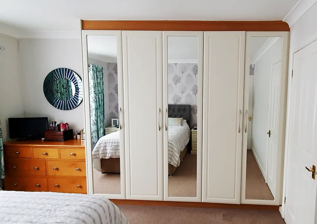 Floor to ceiling bedroom wardrobe in white with mirrored doors.