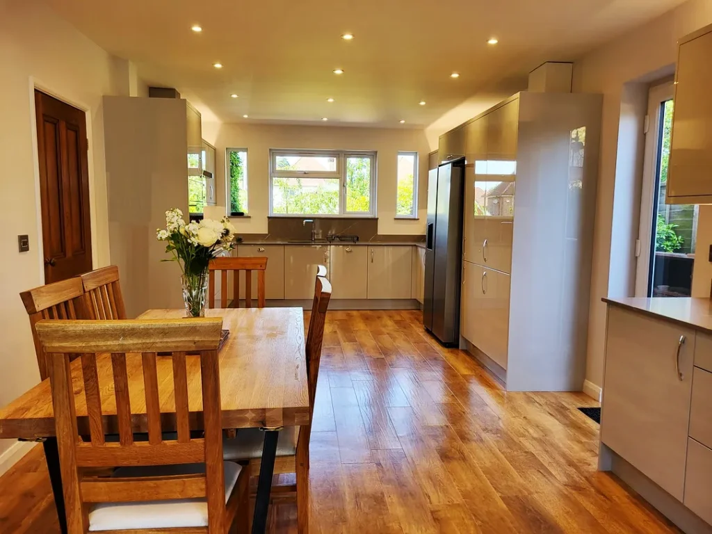 Kitchen with wooden floor, white kitchen units with chrome handles and kitchen table.