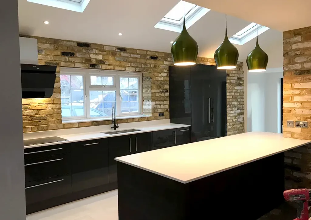 Modern kitchen with black gloss units, white work surfaces and brick walls.