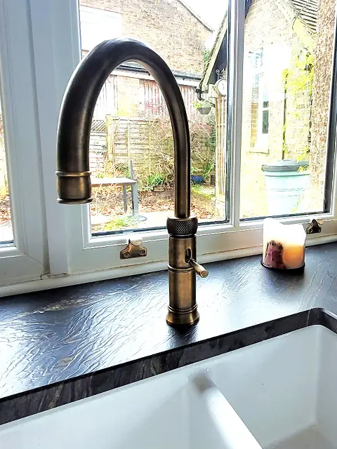 A patinated brass Classic Fusion Quooker tap set in a black granite kitchen work surface.