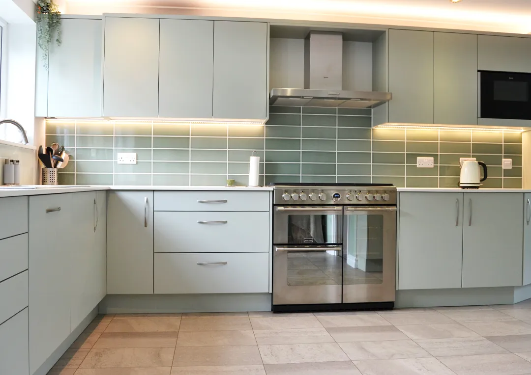 A newly designed and installed Scandinavian-style kitchen with meadow green cabinets, a lightly coloured quartz worktop and stainless steel gas range cooker.