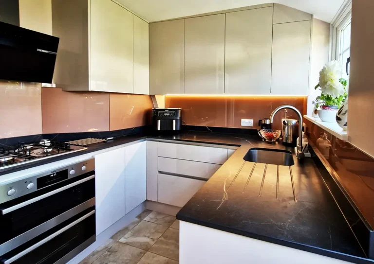 A small modern kitchen with handleless cashmere doors, black ceramic worktops with a copper veining pattern, under cabinet strip lights and a gas hob with angled extractor.