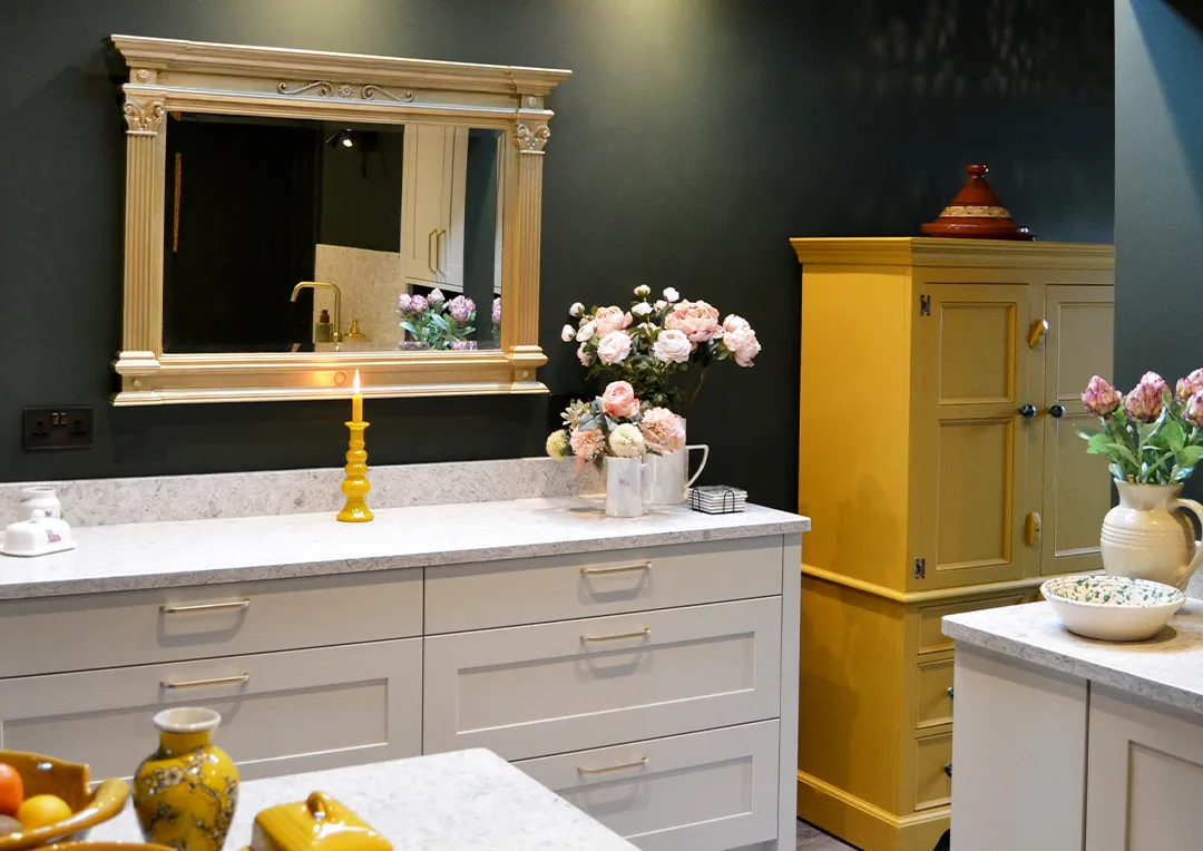Traditional painted shaker style kitchen units painted in mussel with a patterned quartz worktop in a kitchen painted with dark green walls.