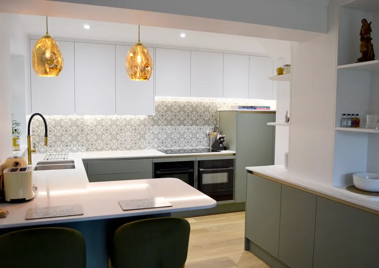 Handleless white and dark green kitchen units, integrated oven and pattern wall tiles.
