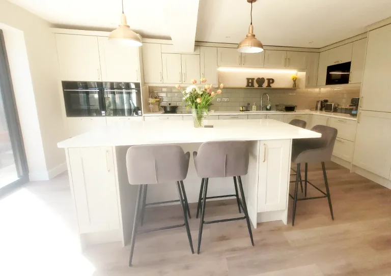 A large open plan shaker style kitchen with a large breakfast bar with seating for four people and large bi-fold patio doors allowing light to flood into the room.
