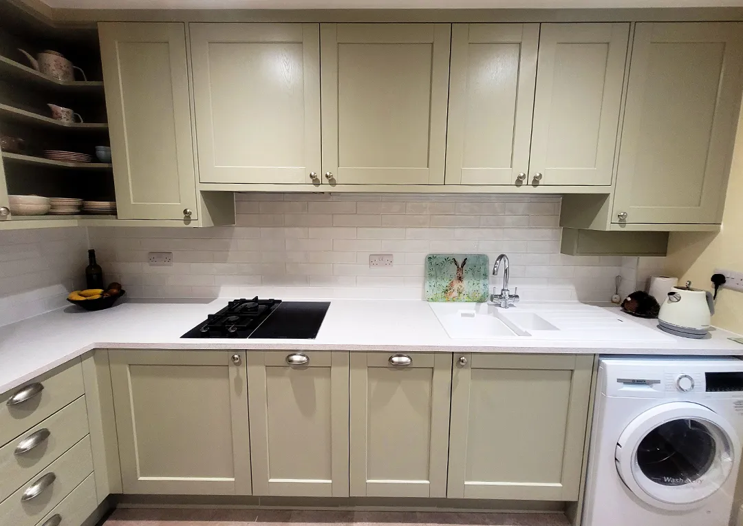 A newly fitted kitchen with sage green shaker doors, white laminate worktop and white metro tiled splashback.