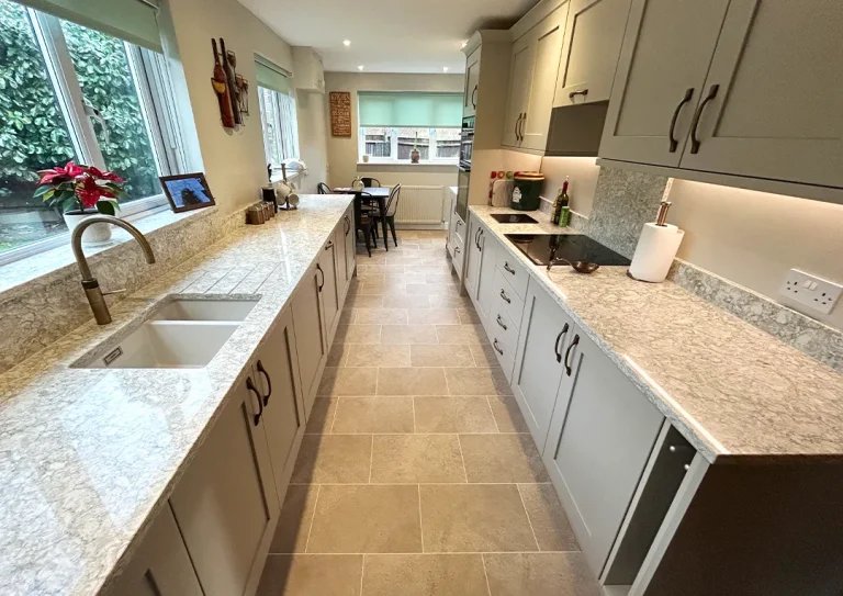 Shaker style kitchen with brass handles, quartz worktop, integrated oven and hob and tile flooring.