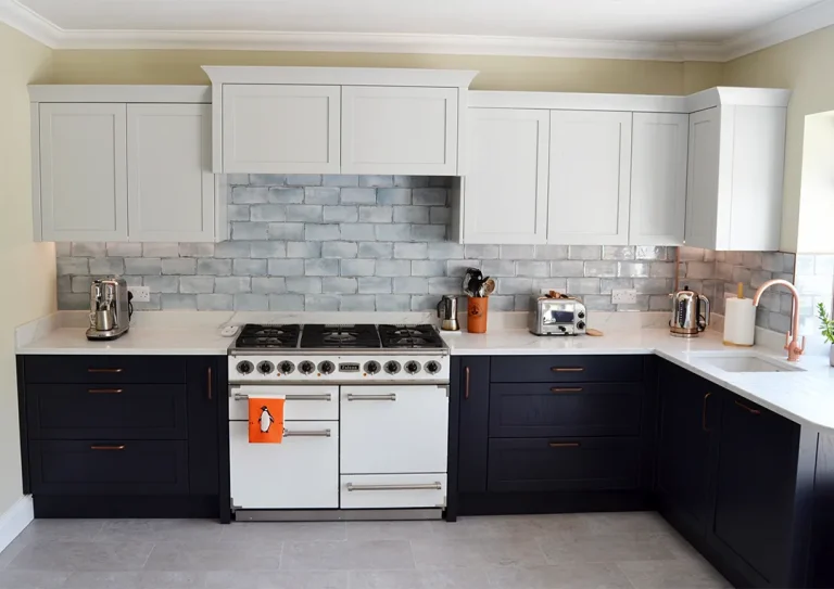 A two tone indigo and light grey shaker style kitchen with handleless and brushed antique copper handles units, Quartz Konigstone Bianco Isola worktops and grey wall tiles.
