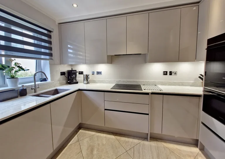 A handleless kitchen in a cashmere colour gloss with black rails, Quartz worktops, glass splashbacks, under cabinet Led lighting and a combination oven and induction hob.