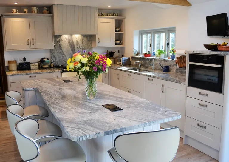 Kitchen with Shaker style doors, chrome handles, large breakfast bar with marble work surface and stools.