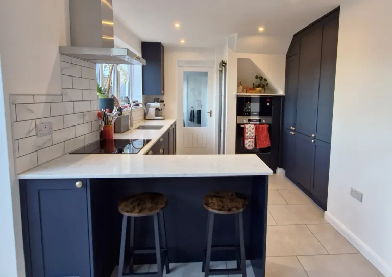 Wide shot of a newly fitted kitchen showing a breakfast bar with two stools. The kithchen is in indigo blue with white marbled quartz worktop.