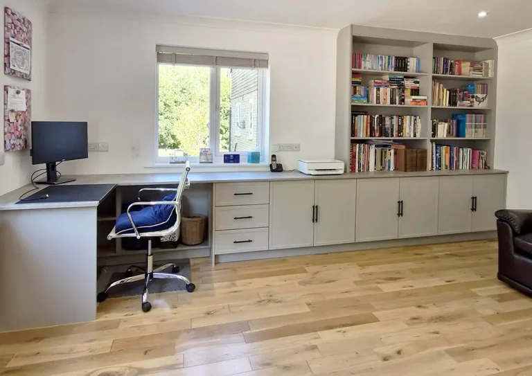 A custom fitted home office in a light grey with desk area, open bookshelves, drawers and lots of built in cupboards.
